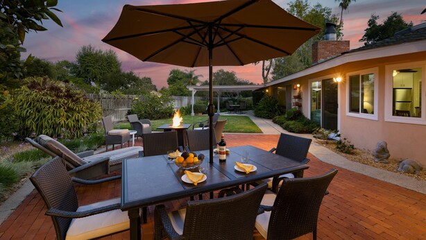 An outdoor patio with a dining table, chairs, and a large umbrella. - East Valley Manor by Avantstay Minutes to the Beach (Santa Barbara)