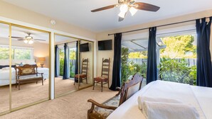 A bedroom with a large mirror, a ceiling fan, a bed with a white comforter, a wooden chair, and a view of the outdoors. - East Valley Manor by Avantstay Minutes to the Beach (Santa Barbara)