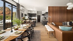 A modern kitchen with dark cabinets, a dining area with a long table set for six, and a cozy seating area with a leather couch and cushions. - Roca Roja by Avantstay Mountain Views in the Heart of Sedona (Sedona)