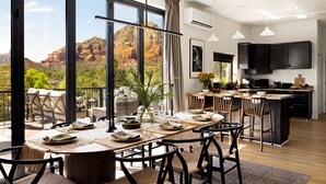 A modern kitchen with dark cabinets and a large island, a dining area with a view of red rock formations, and a balcony with outdoor seating. - Roca Roja by Avantstay Mountain Views in the Heart of Sedona (Sedona)