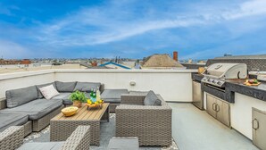 A rooftop terrace with outdoor seating, a grill, and a view of the city. - Seaside Style by Avantstay Rooftop Walk to Beach Chic Design (Newport Beach)