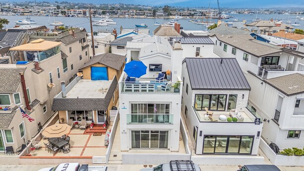 A residential area with modern houses, a patio with outdoor furniture, and a marina in the background. - Seaside Style by Avantstay Rooftop Walk to Beach Chic Design (Newport Beach)