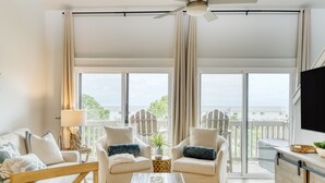 Ein geräumiges Wohnzimmer mit großem Fenster, Deckenventilator und Flachbildfernseher.