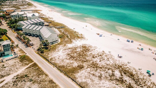 Luftaufnahme eines an der Küste gelegenen Hotels mit mehreren Gebäuden, einem Strand und einer Straße.