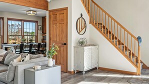 A spacious living area with a wooden staircase, a dining area, and a large window offering a view of the outdoors.