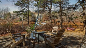 A wooden deck with a fire pit and chairs, surrounded by trees and a body of water.