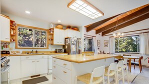 Une cuisine moderne avec des meubles blancs, un plan de travail en bois et une grande fenêtre donnant sur un jardin.