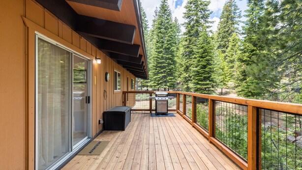 Une terrasse en bois avec un barbecue, des portes-fenêtres coulissantes et une vue sur de grands arbres.
