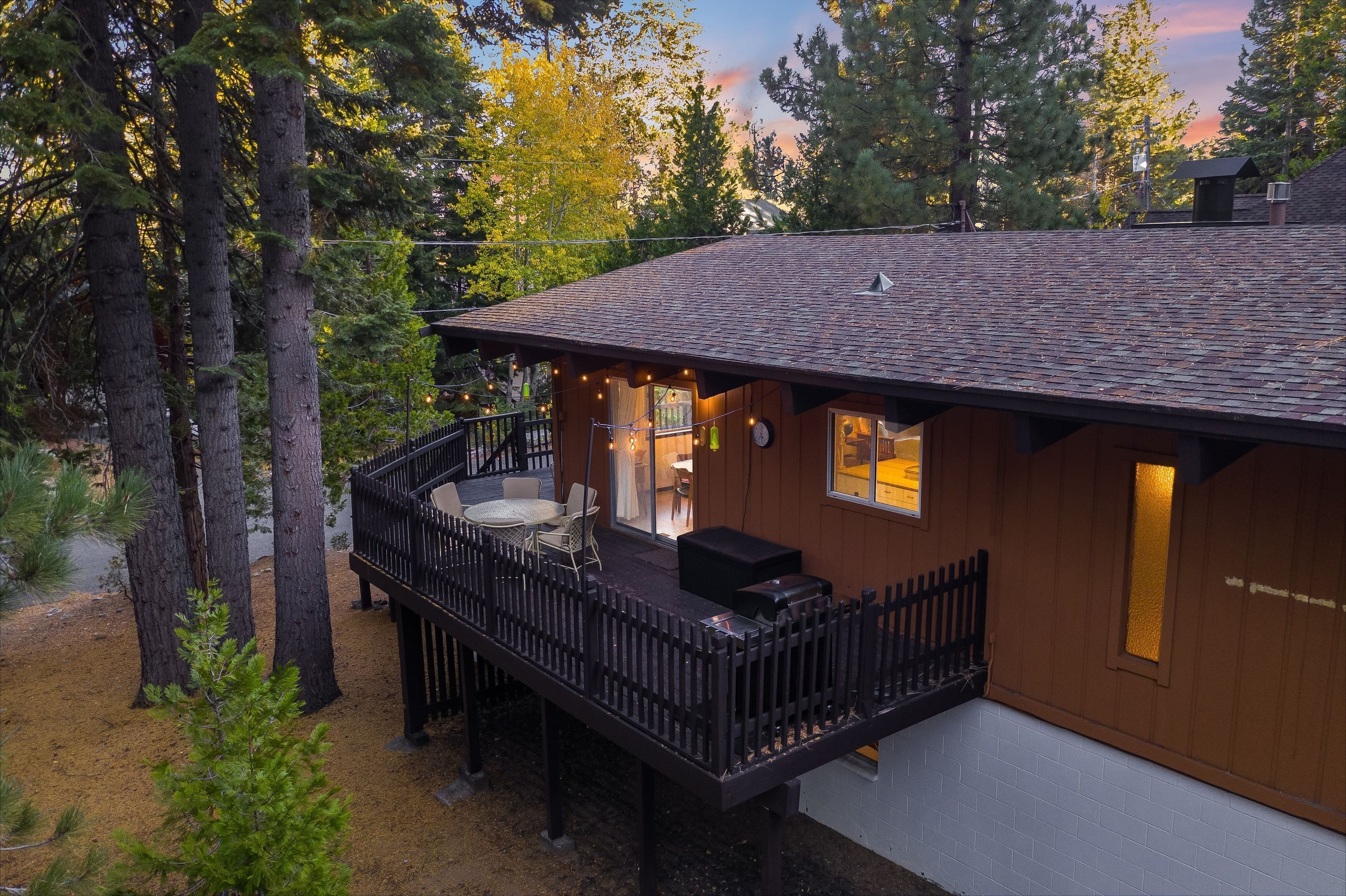 A cabin with a deck, outdoor seating, and a view of the surrounding forest.