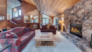 Ein gemütliches Wohnzimmer mit Kamin aus Stein, Holzboden und großen Fenstern.