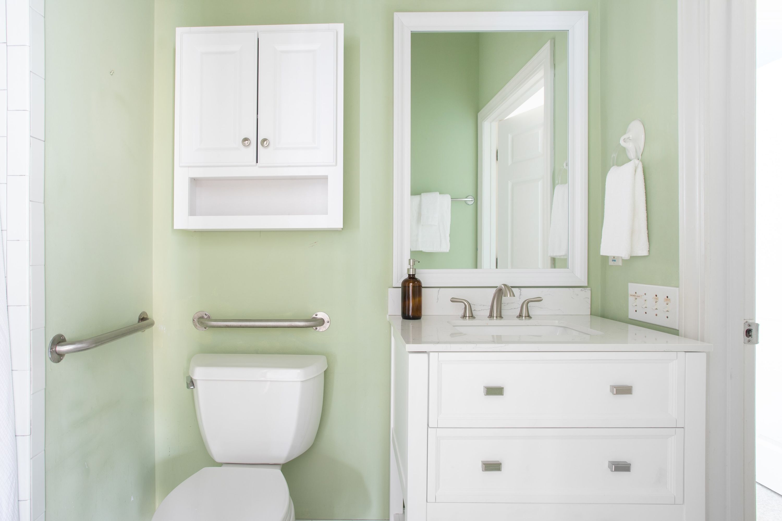 A bathroom with a toilet, a sink, a mirror, and a cabinet.