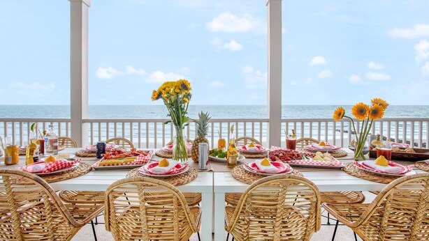 A table set for a meal with a view of the sea, wicker chairs, and a white tablecloth. - Poseidon By Avantstay On The Beach Two Ocean Facing Balconies Hot Tub (Folly Beach)