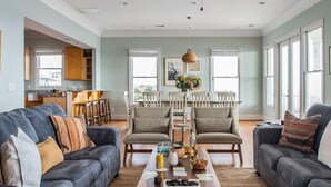 A spacious living room with a dark grey sofa, a wooden coffee table with snacks, and a dining area with a white table and chairs. - Poseidon By Avantstay On The Beach Two Ocean Facing Balconies Hot Tub (Folly Beach)