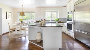 A modern kitchen with white cabinets, a central island, stainless steel appliances, and a dining area with a table and chairs. - Wildflower by Avantstay Gorgeous Wine Country Home w Pool Bocce Ball Court Huge Yard (Sonoma)