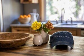 A wooden bowl, two ceramic vases with flowers, and a cap on a wooden table.
