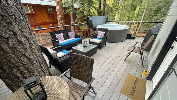 Una terraza exterior con mobiliario de mimbre, un jacuzzi y una cabaña de madera al fondo.
