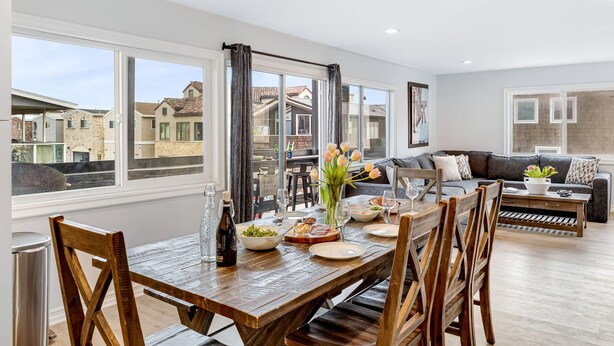 A spacious living area with a dining table set for a meal, a sofa, and a view of neighboring houses. - Shelly by Avantstay Steps to the Beach Deck w Ocean Views 5bdr (Newport Beach)