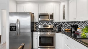 A modern kitchen with stainless steel appliances, white cabinetry, and a patterned backsplash. - Shelly by Avantstay Steps to the Beach Deck w Ocean Views 5bdr (Newport Beach)
