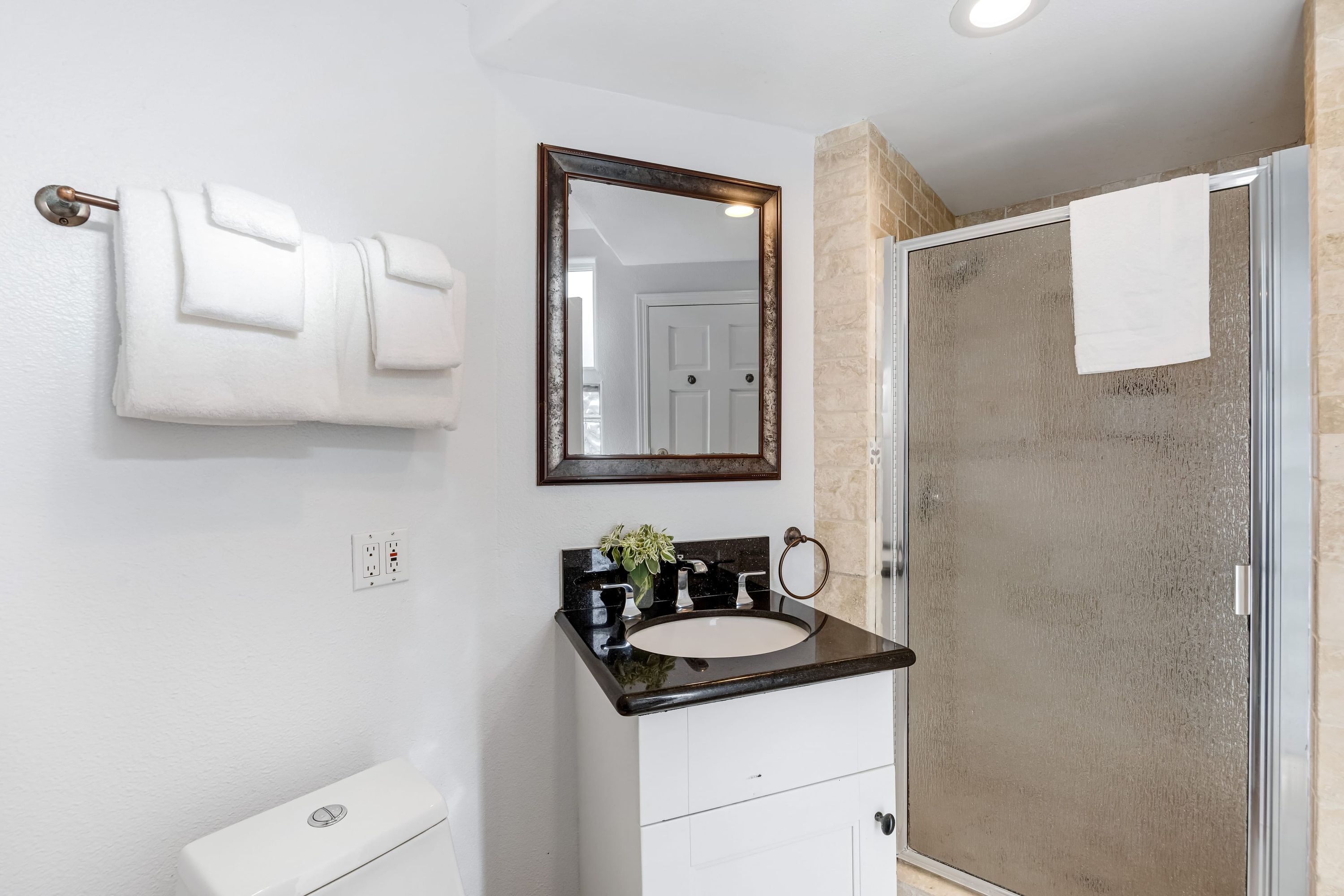 Un baño con inodoro blanco, lavamanos negro, espejo y cabina de ducha de vidrio.