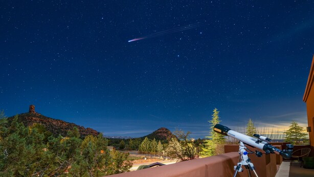 Ein Teleskop auf einem Balkon mit Blick auf eine Berglandschaft bei Nacht.