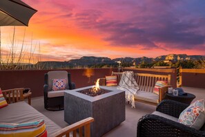 An outdoor patio with a fire pit, seating, and a view of mountains during sunset.