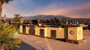 An outdoor kitchen area with a stone counter, built-in cabinets, and a grill, overlooking a mountainous landscape.