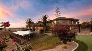 A two-story house with a covered patio, palm trees, and a well-maintained lawn.