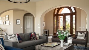 A spacious living room with a grey sofa, a brown leather armchair, and a wooden coffee table with a vase of flowers.