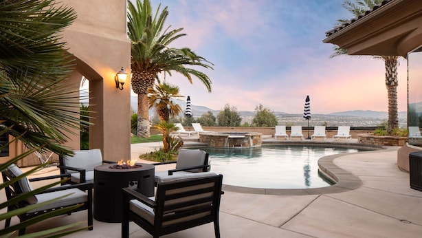 A pool area with lounge chairs, a fire pit, and a view of the mountains.
