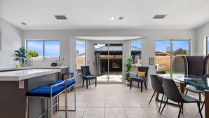 A spacious kitchen with a bar area, large windows, and a patio with outdoor seating. - Pacifica Sur by Avantstay Pool Hot Tub Gazebo (Indio)