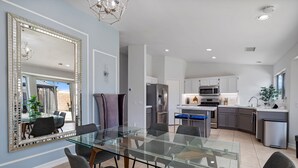 A modern kitchen with white cabinets, stainless steel appliances, and a glass dining table. - Pacifica Sur by Avantstay Pool Hot Tub Gazebo (Indio)