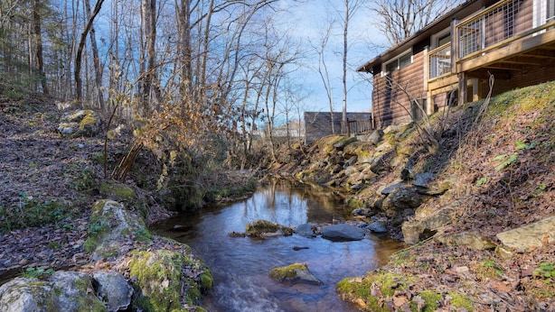 A wooden cabin with a stone foundation, a small stream, and a forested area. - Creekside Haven Gatlinburg Escape by a Bubbling Creek Near Top Attractions (Gatlinburg)