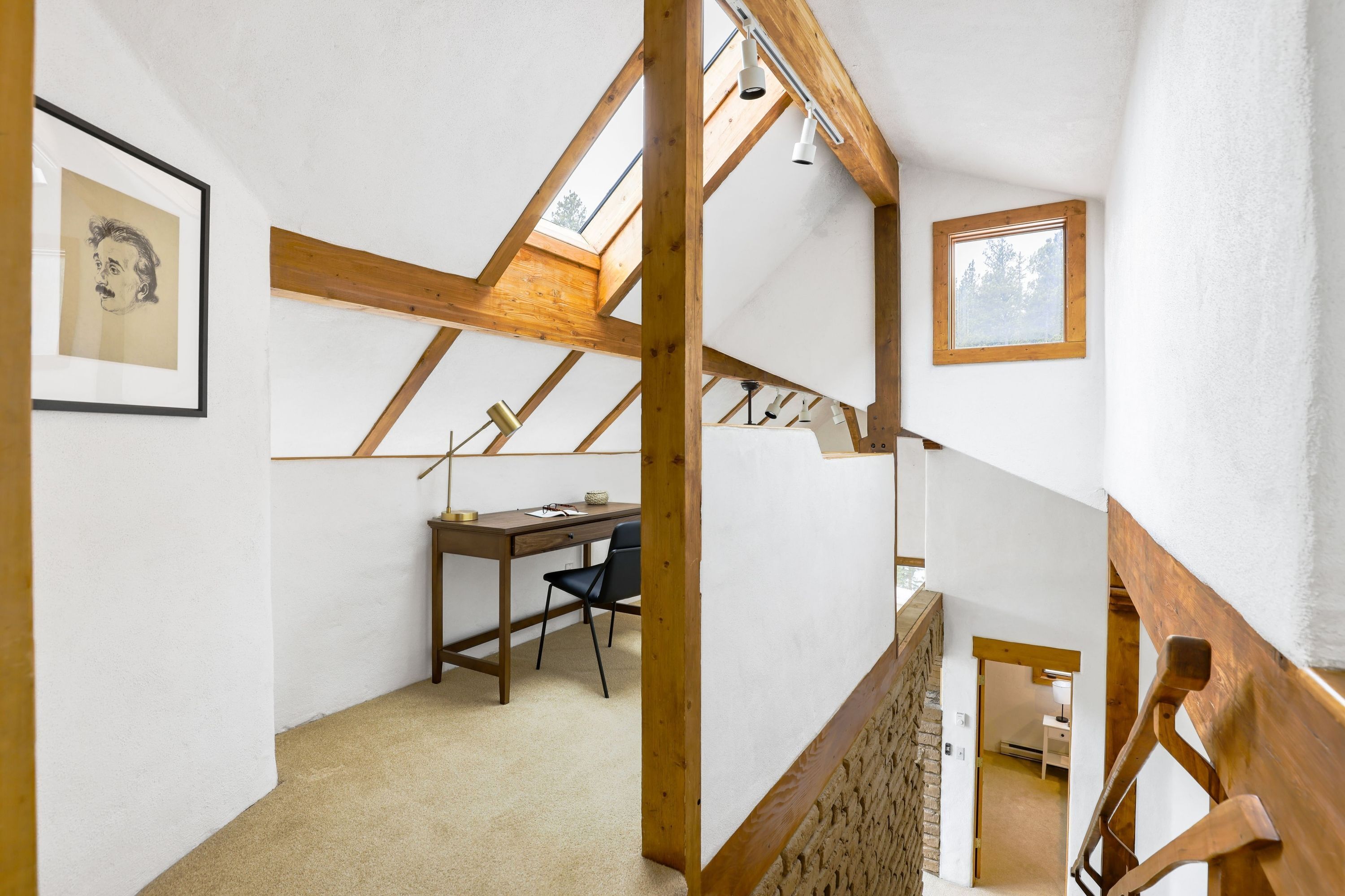 A room with a sloped ceiling, wooden beams, a desk, and a chair.