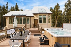 Une terrasse dotée d’un jacuzzi, de chaises longues en bois, d’une table avec des chaises et d’un espace couvert comprenant une table et des chaises.