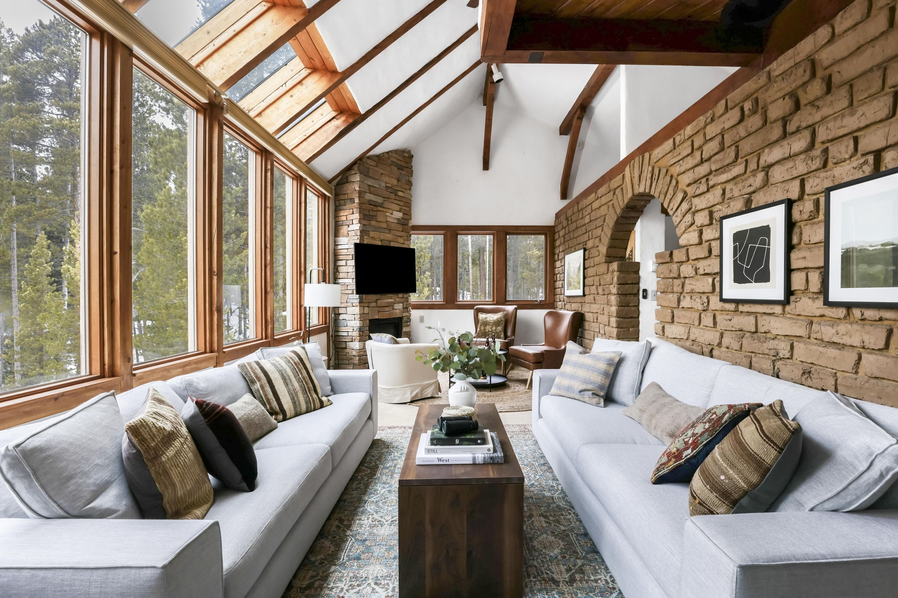 A spacious living room with a large window, a fireplace, and a stone wall.