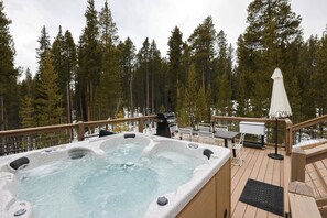 Un bain à remous sur une terrasse en bois, avec vue sur de grands pins.