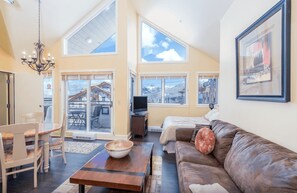 A spacious living room with a large brown leather couch, a wooden coffee table, and a chandelier. There is a television and a fireplace in the background. - Blue Mesa Penthouse by Avantstay Buyout of 3 Units Ski-in Ski-out Condo (Telluride)
