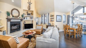 A spacious living room with a fireplace, leather sofas, a dining area with wooden chairs, and a large window offering a view. - Blue Mesa Penthouse by Avantstay Buyout of 3 Units Ski-in Ski-out Condo (Telluride)
