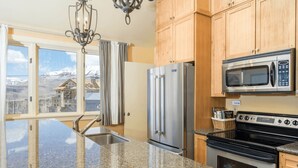 A kitchen with granite countertops, stainless steel appliances, wooden cabinets, and a view of a mountainous landscape through large windows. - Blue Mesa Penthouse by Avantstay Buyout of 3 Units Ski-in Ski-out Condo (Telluride)