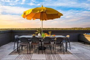 Una terraza en la azotea con mesa y sillas, una sombrilla y vistas al paisaje.