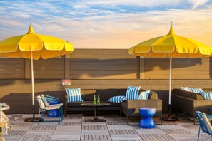 Un área de lounge en la azotea con sombrillas amarillas, un conjunto de sofás y una mesa con botellas.