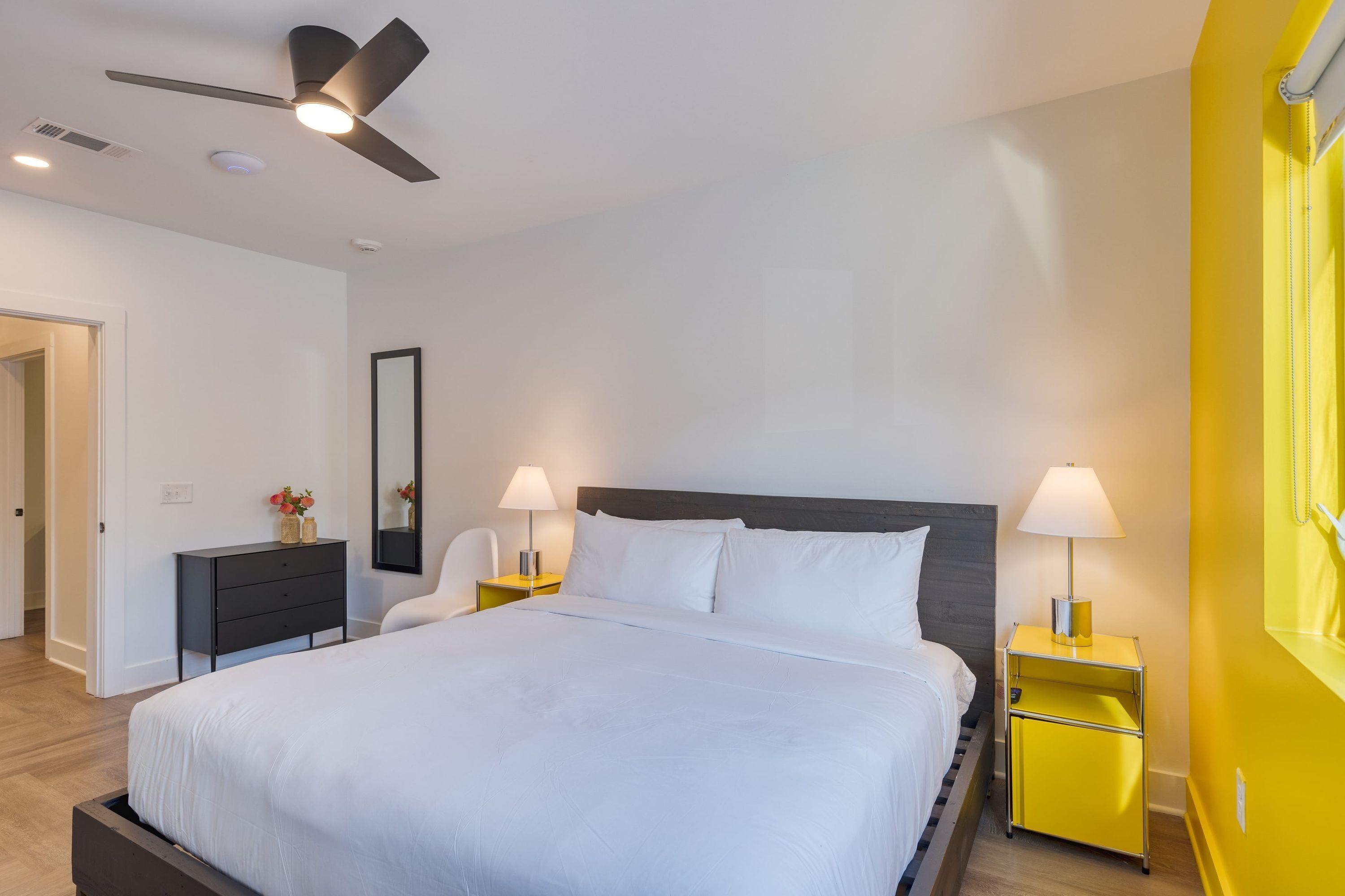 A modern bedroom with a large bed, two bedside tables with lamps, a ceiling fan, and a wooden nightstand.