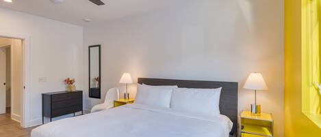 A modern bedroom with a large bed, two bedside tables with lamps, a ceiling fan, and a wooden nightstand.