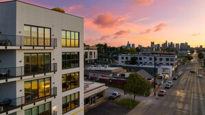 A multi-story building with balconies, a parking lot, and a city skyline in the background.