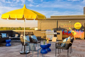 Una terraza en la azotea con mobiliario exterior, una parrilla y un mural.