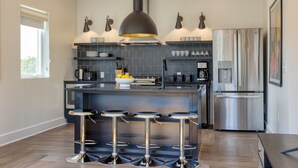 A modern kitchen with a central island, bar stools, a stainless steel refrigerator, and a pendant light.