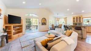A spacious living room with a large sofa, a flat-screen TV, and a dining area with chairs and a table. - Blitzen by Avantstay Pet-friendly Tahoe Retreat (South Lake Tahoe)