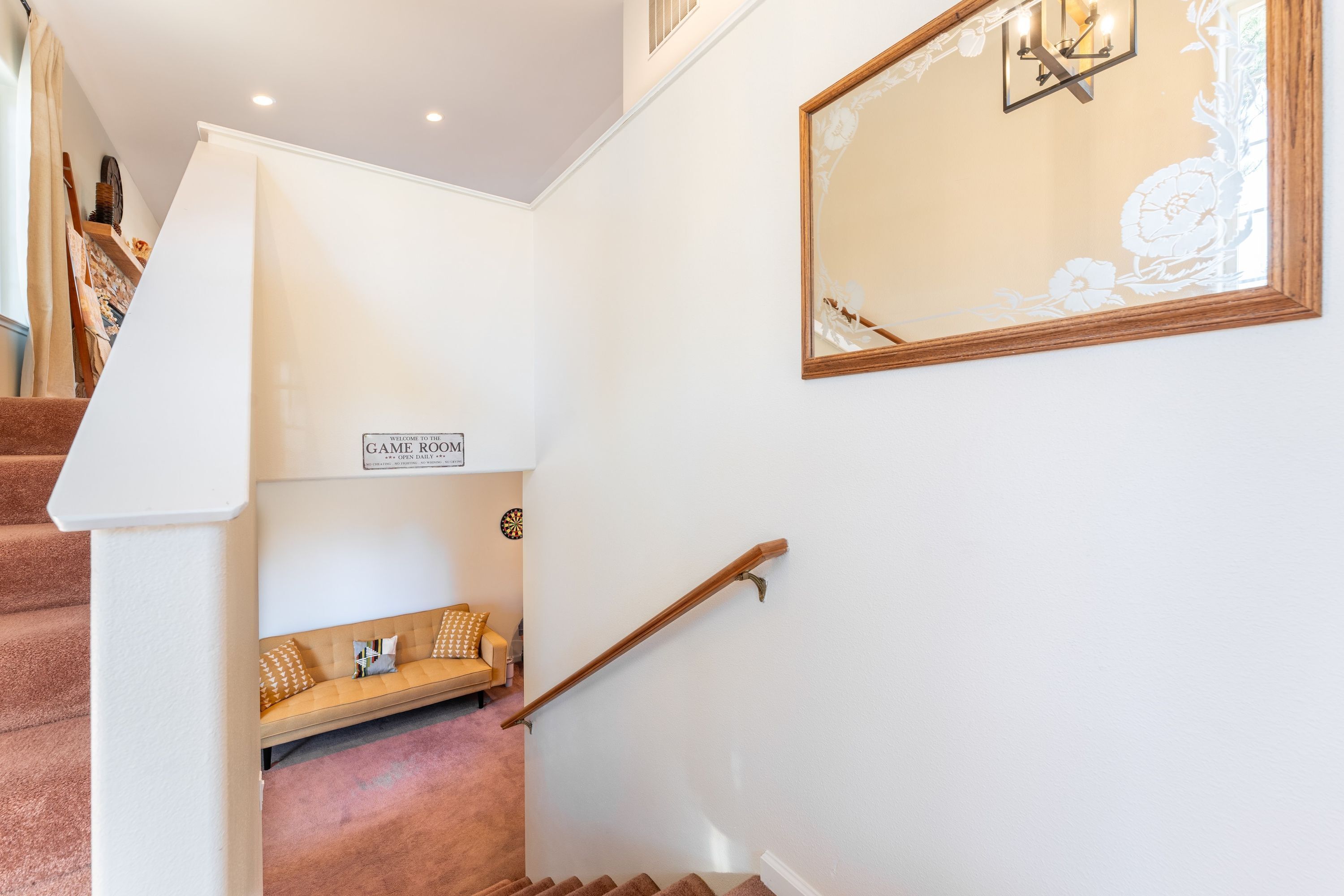 A staircase with a wooden handrail, a bench with patterned cushions, and a sign reading "GAME ROOM" in a corner.