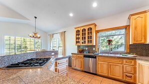 A kitchen with granite countertops, wooden cabinets, a stainless steel dishwasher, and a window with a view of trees. - Blitzen by Avantstay Pet-friendly Tahoe Retreat (South Lake Tahoe)