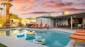 Une piscine entourée de palmiers et d’un bâtiment doté d’une terrasse, avec des chaises longues et des parasols à proximité.